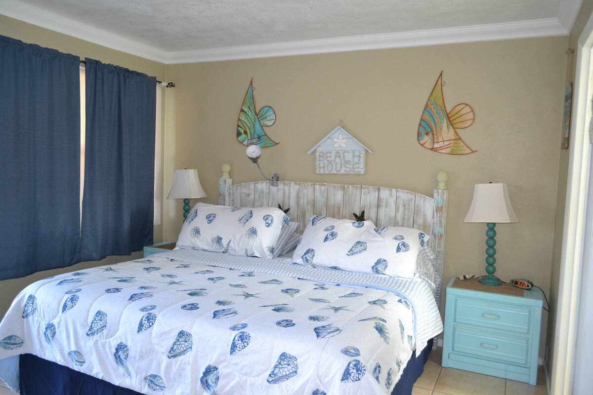 A bedroom with a bed, two nightstands, a wall clock, and decorative wall art.