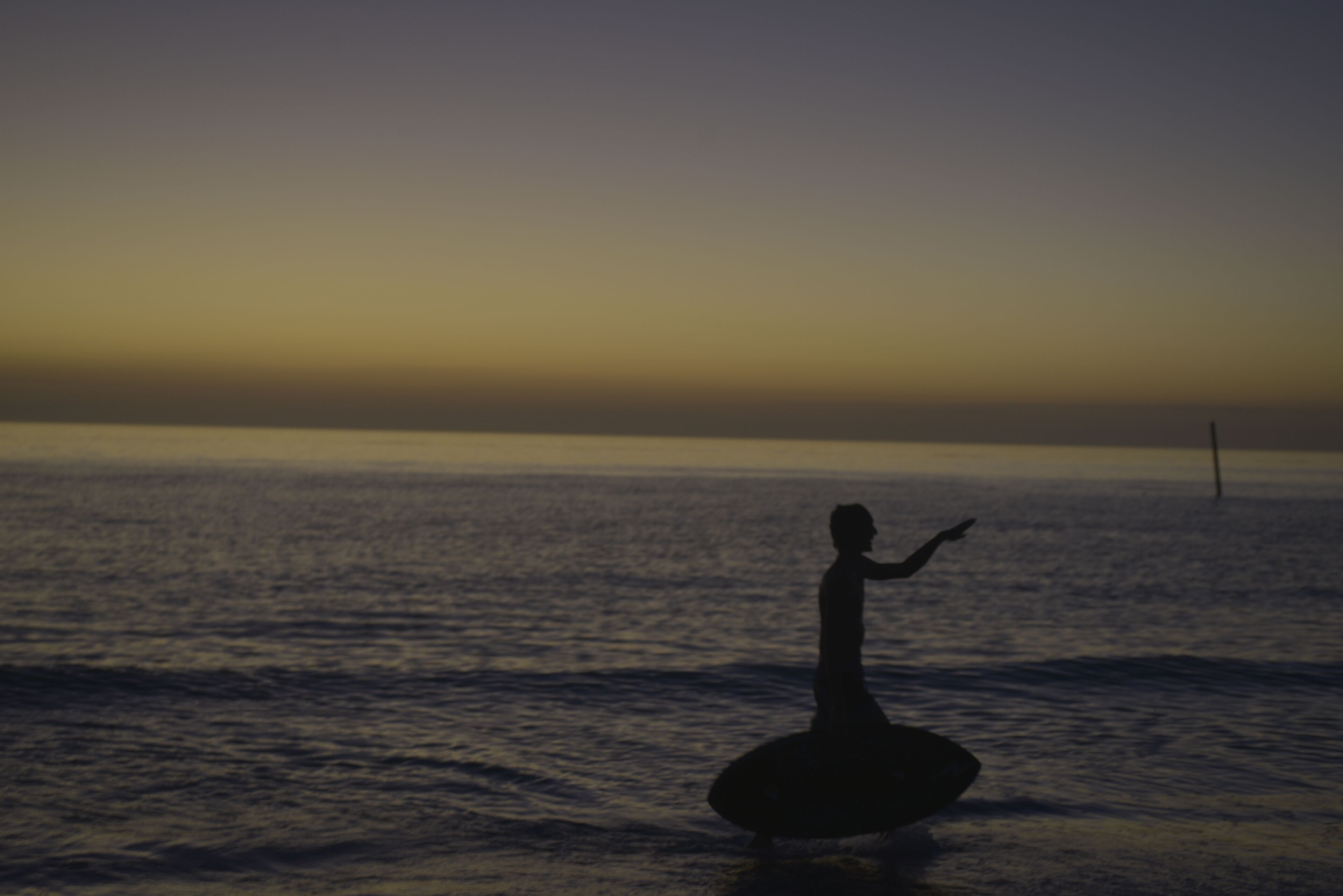 A silhouette of a person on a surfboard against a sunset over the ocean.