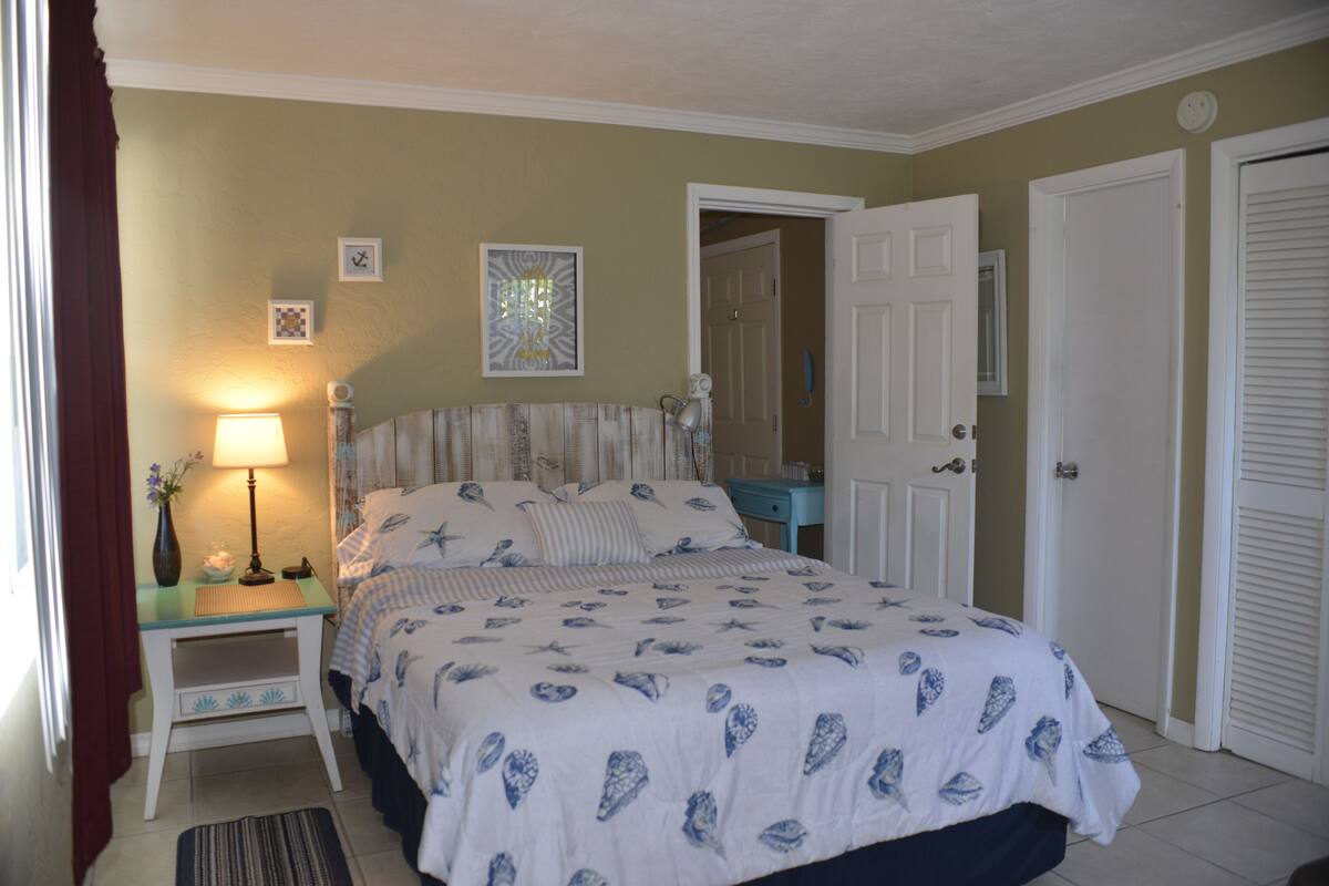 A bedroom with a bed, nightstand, lamp, and a door.