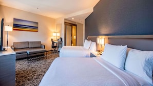 Ein Hotelzimmer mit zwei Betten, einer Couch, einem Schreibtisch und einer Lampe.