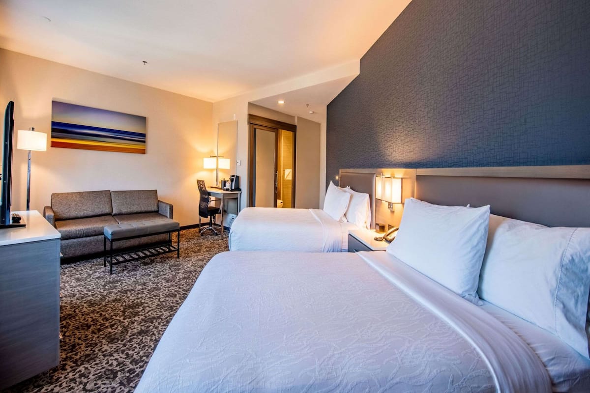 Ein Hotelzimmer mit zwei Betten, einer Couch, einem Schreibtisch und einer Lampe.