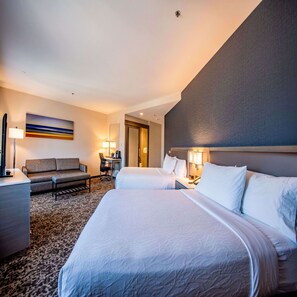 Habitación de hotel con dos camas, un sofá, un escritorio y una lámpara.