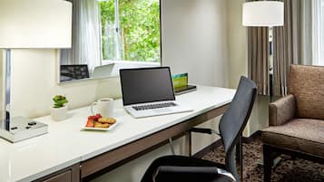 A hotel room with a desk, laptop, coffee cup, plate of cookies, and a chair.