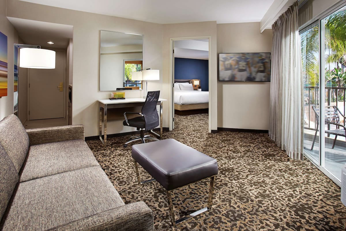 Ein Hotelzimmer mit einer Couch, einem Schreibtisch mit Stuhl, einem Bett, einem großen Spiegel und Blick ins Freie.