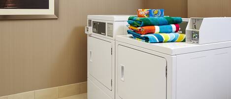 A laundry area with stacked colorful towels and a box of Bounce detergent.