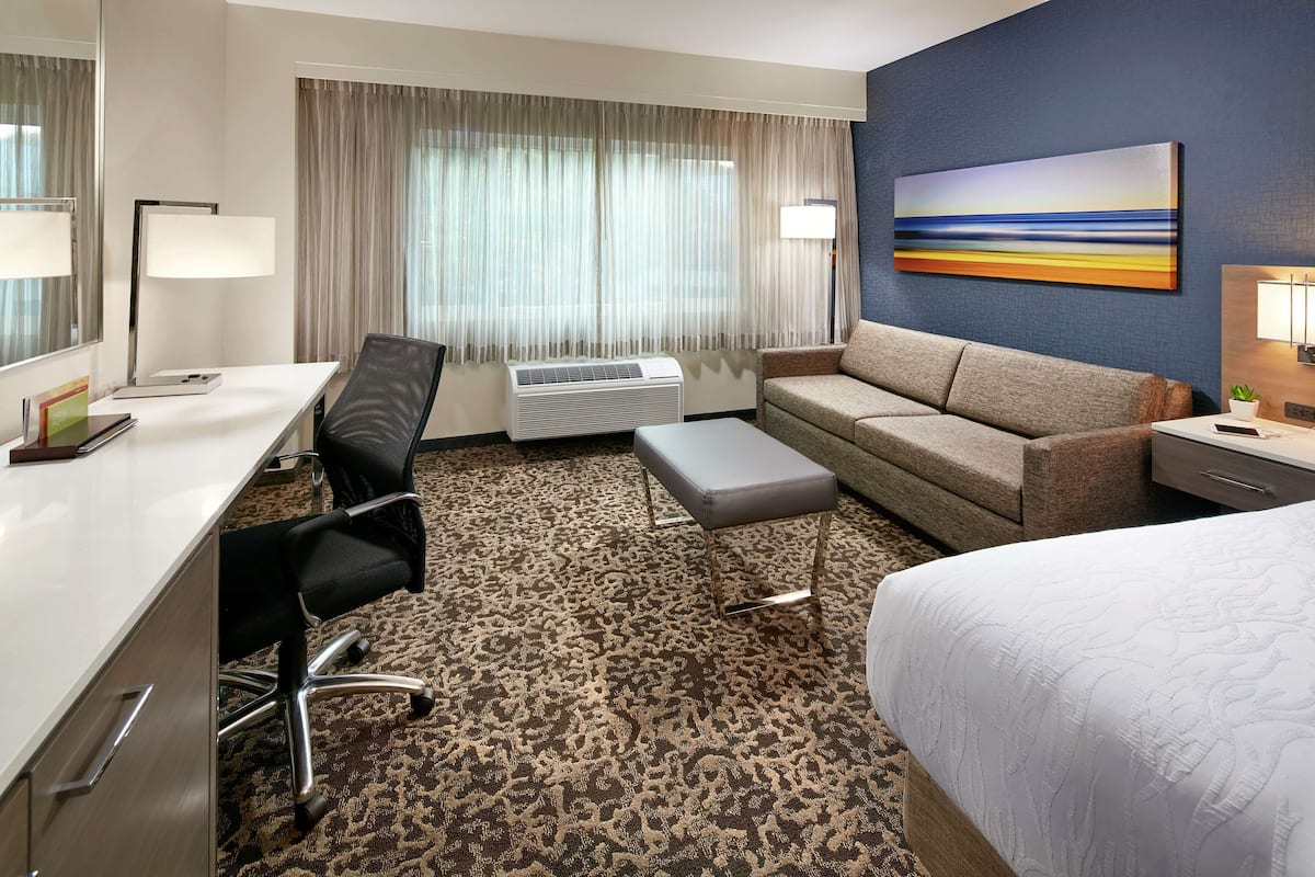 Ein Hotelzimmer mit Schreibtisch, Stuhl, Sofa und Bett.