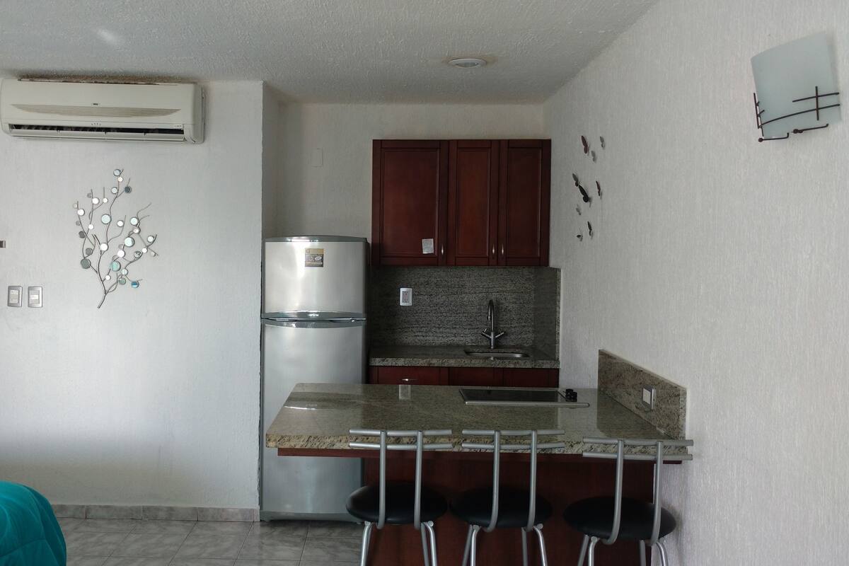 Una cocina compacta con refrigerador, pileta y un elemento decorativo en la pared.