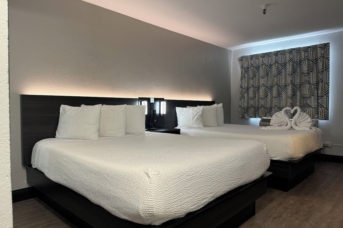 A hotel room with two beds, each with white bedding and a dark headboard. There is a patterned wall behind the beds and a window with a geometric design.