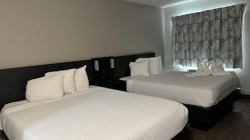 A hotel room with two beds, a dark headboard, and a window with patterned curtains.