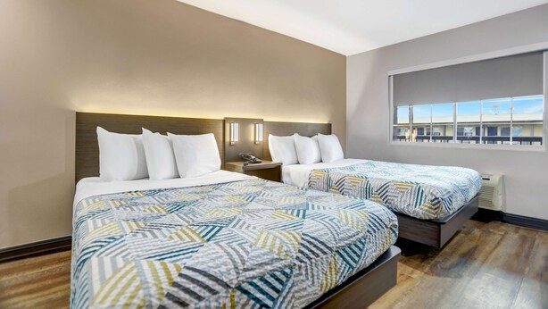 Habitación de hotel con dos camas, un ventanal grande y vistas al edificio de afuera.