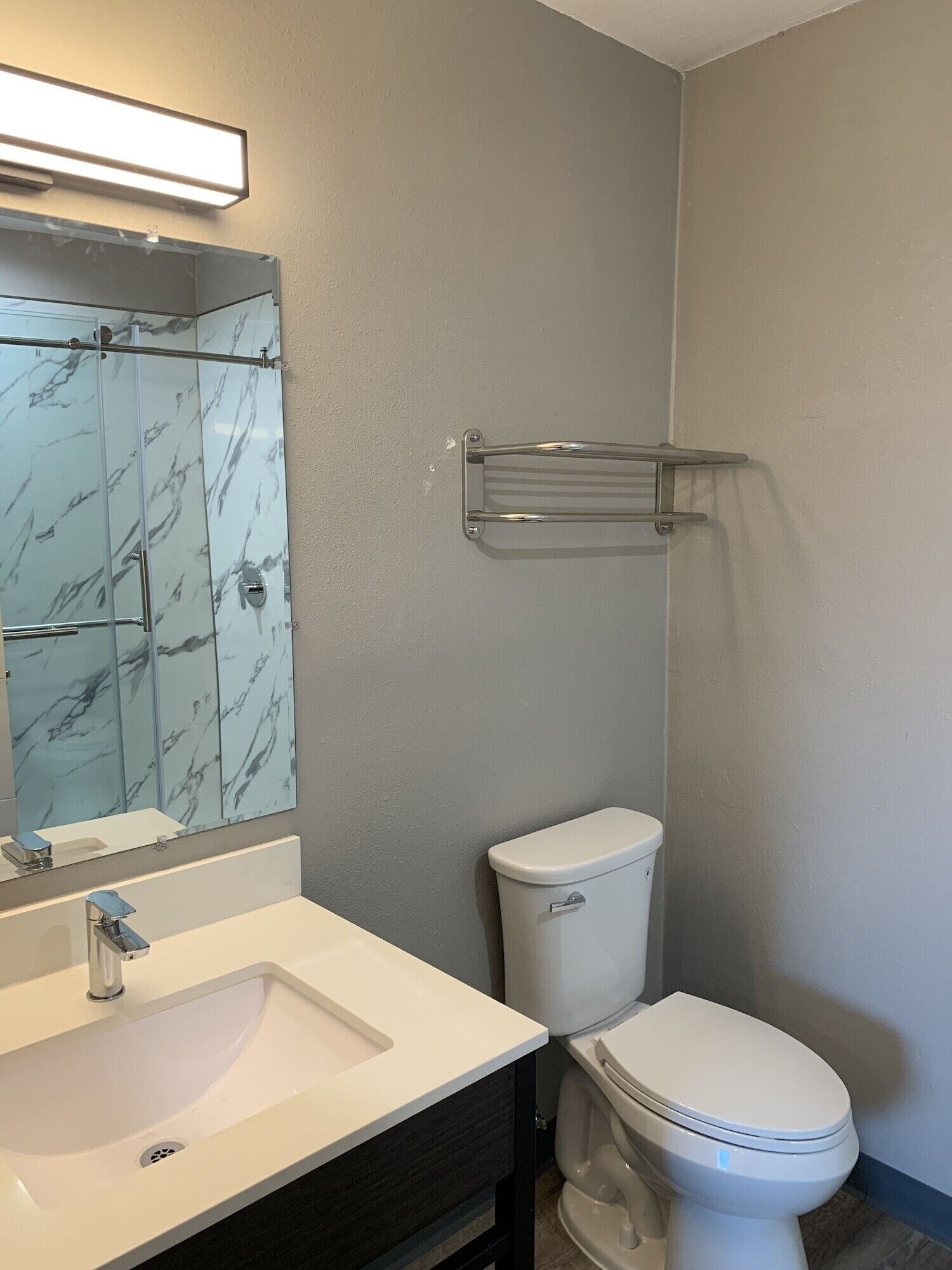 Une salle de bain avec un lavabo blanc, un miroir avec un pare-éclaboussures en marbre, des toilettes et un porte-serviettes.