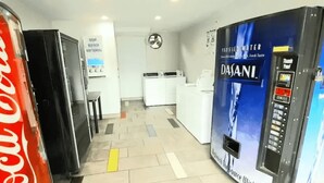 Un vestíbulo de hotel con un refrigerador de Coca-Cola, un dispensador de agua Dasani y un letrero que indica la disponibilidad de jabón y lejía.
