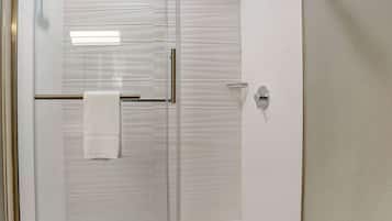 A glass-enclosed shower with a white towel hanging on a metal bar.