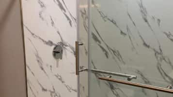 En dusch med glasväggar och en vägg av marmor.