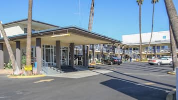 Un motel con entrada techada, palmeras y un estacionamiento lleno de coches.