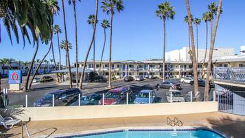 A hotel with a pool, palm trees, and a parking lot.