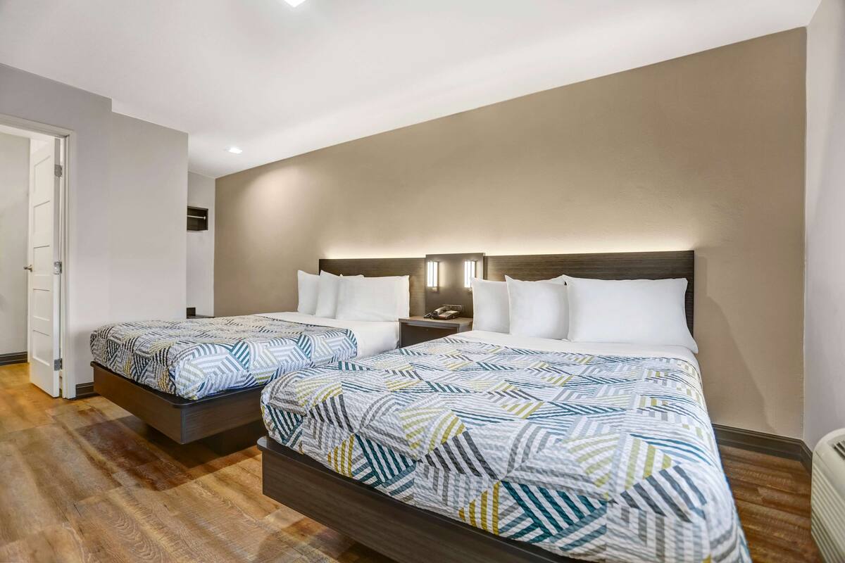 Ett hotellrum med två sängar, trägolv, en vit dörr och en beige vägg.