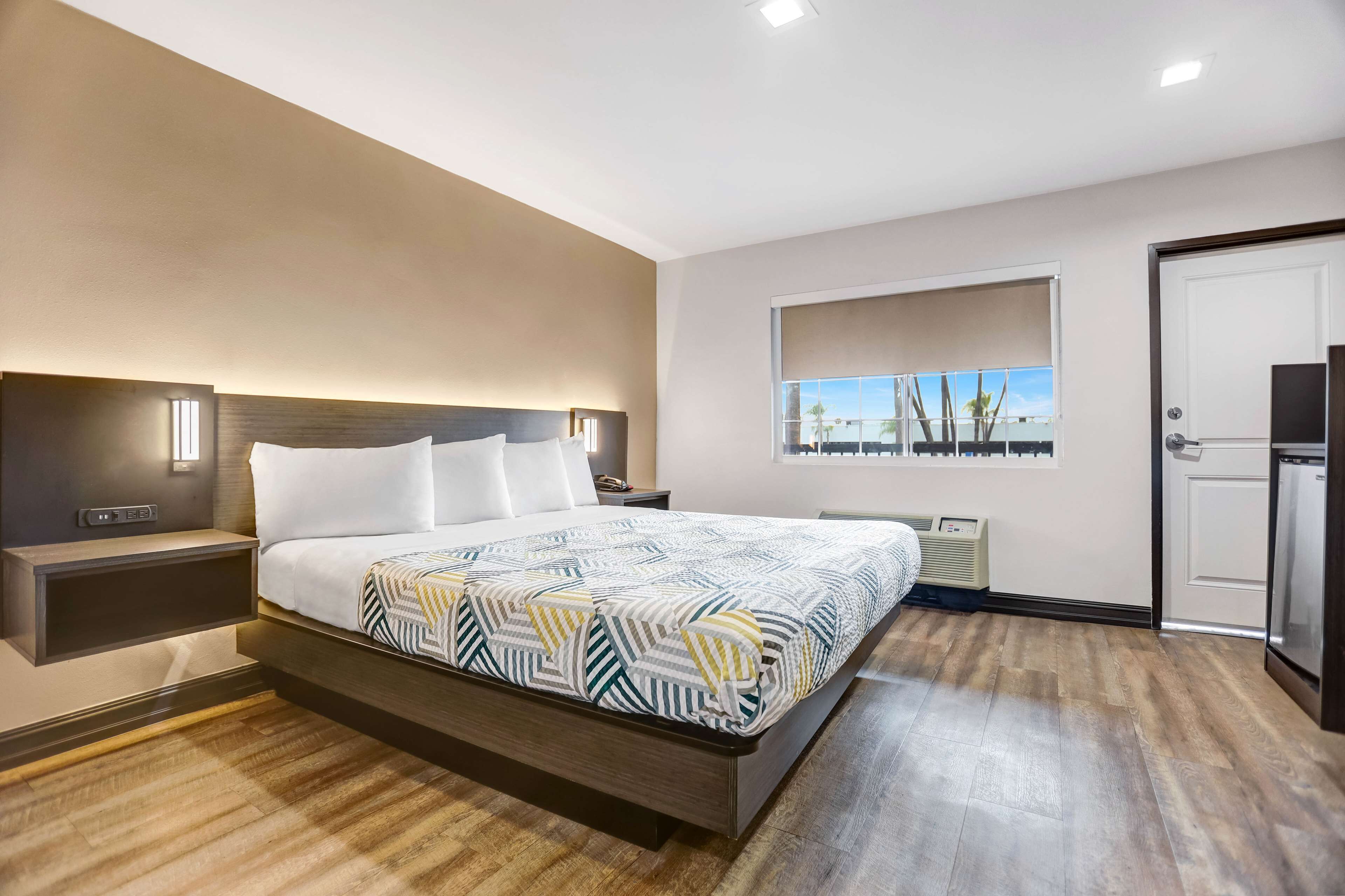 Une chambre moderne avec un grand lit, une table de chevet, une étagère intégrée, une fenêtre donnant sur un beau paysage et une porte menant à la salle de bain.