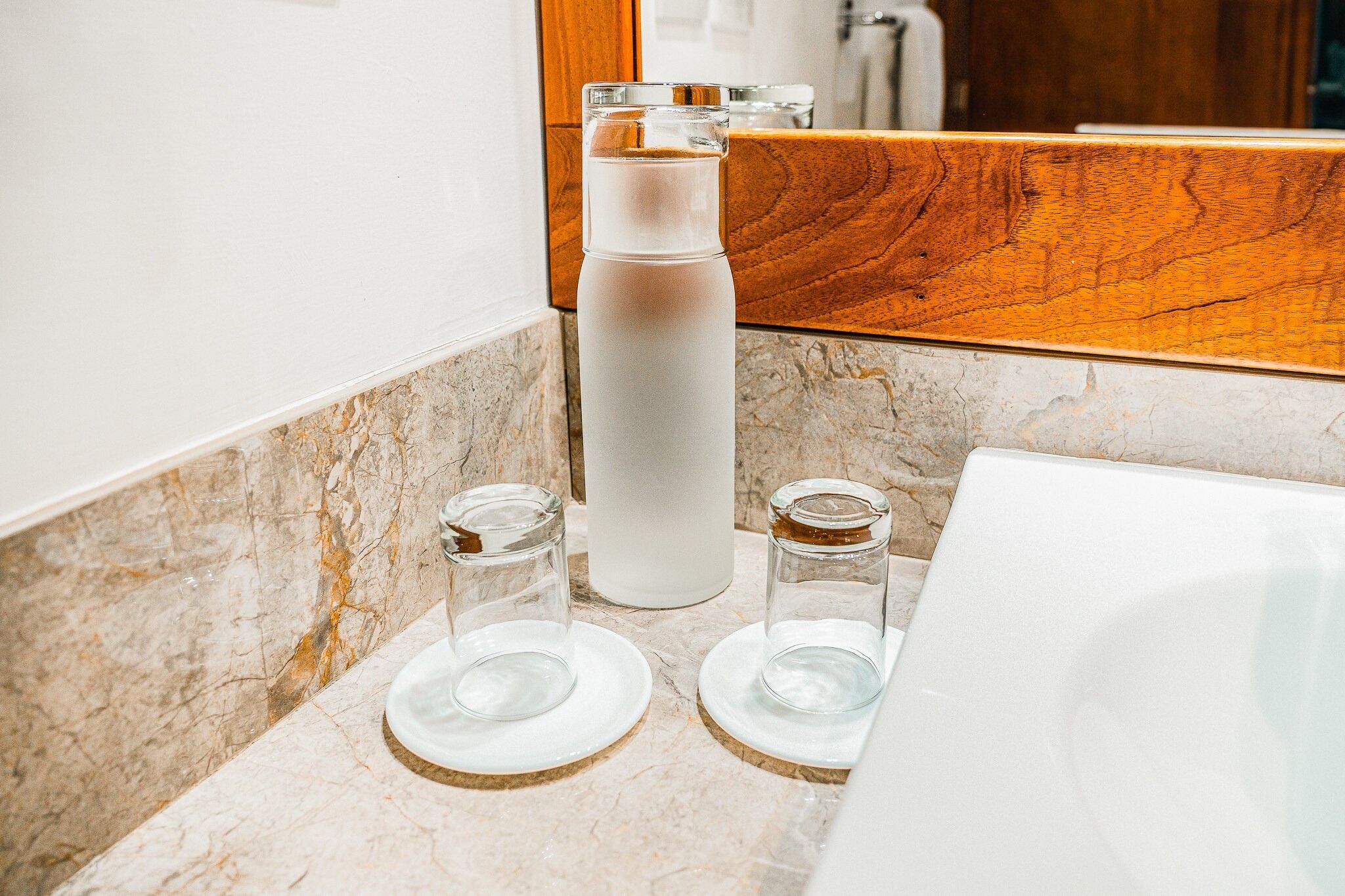 A bathroom with a marble countertop, a white bottle, and two glass containers.
