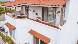 En hvid bygning med røde tegltag, store vinduer og en balkon med fletningsmøbler.