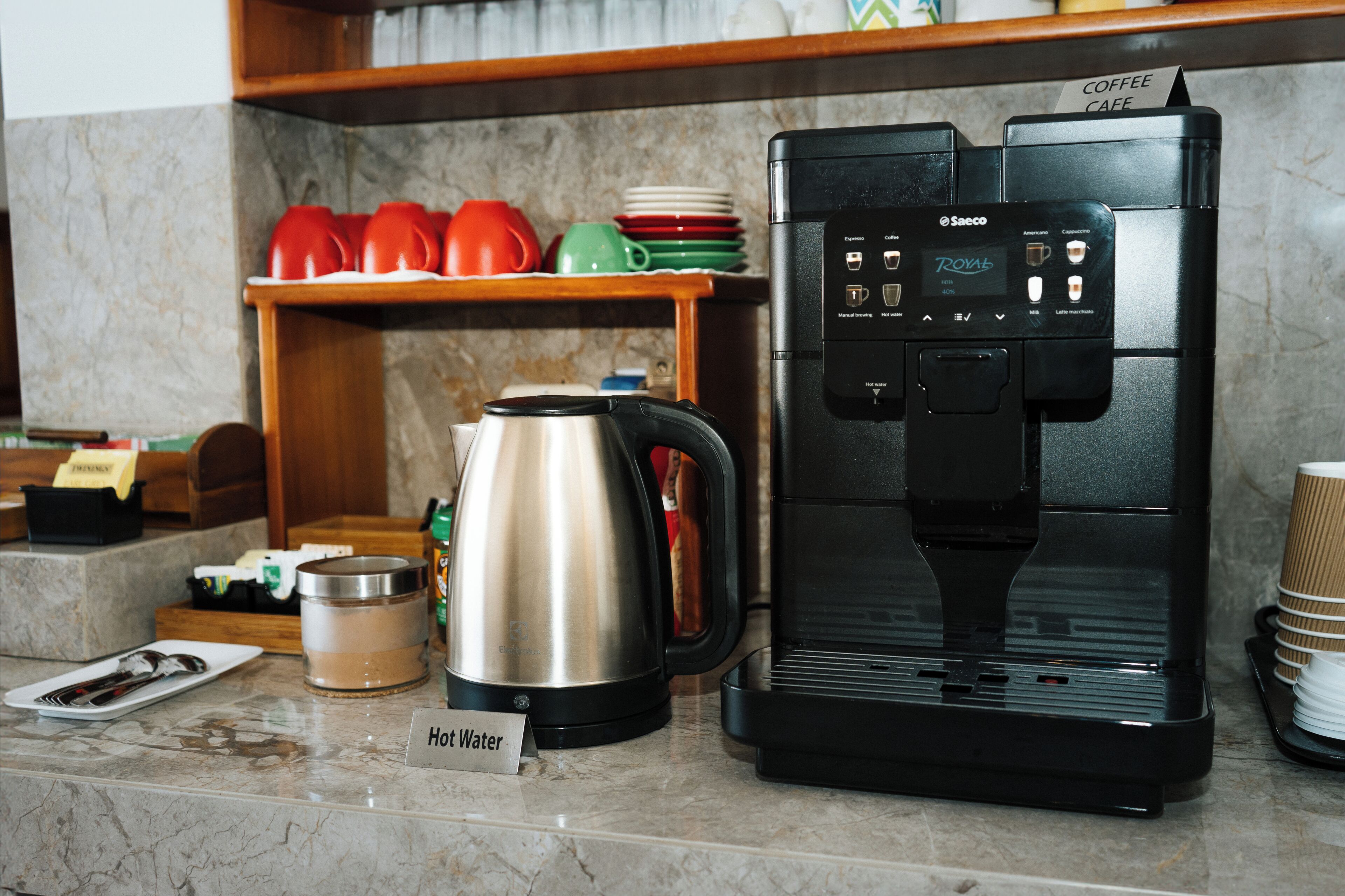 A coffee machine with a hot water dispenser, a stainless steel electric kettle, and a coffee cup holder on a marble countertop.