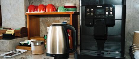 A coffee machine with a hot water dispenser, a stainless steel electric kettle, and a coffee cup holder on a marble countertop.