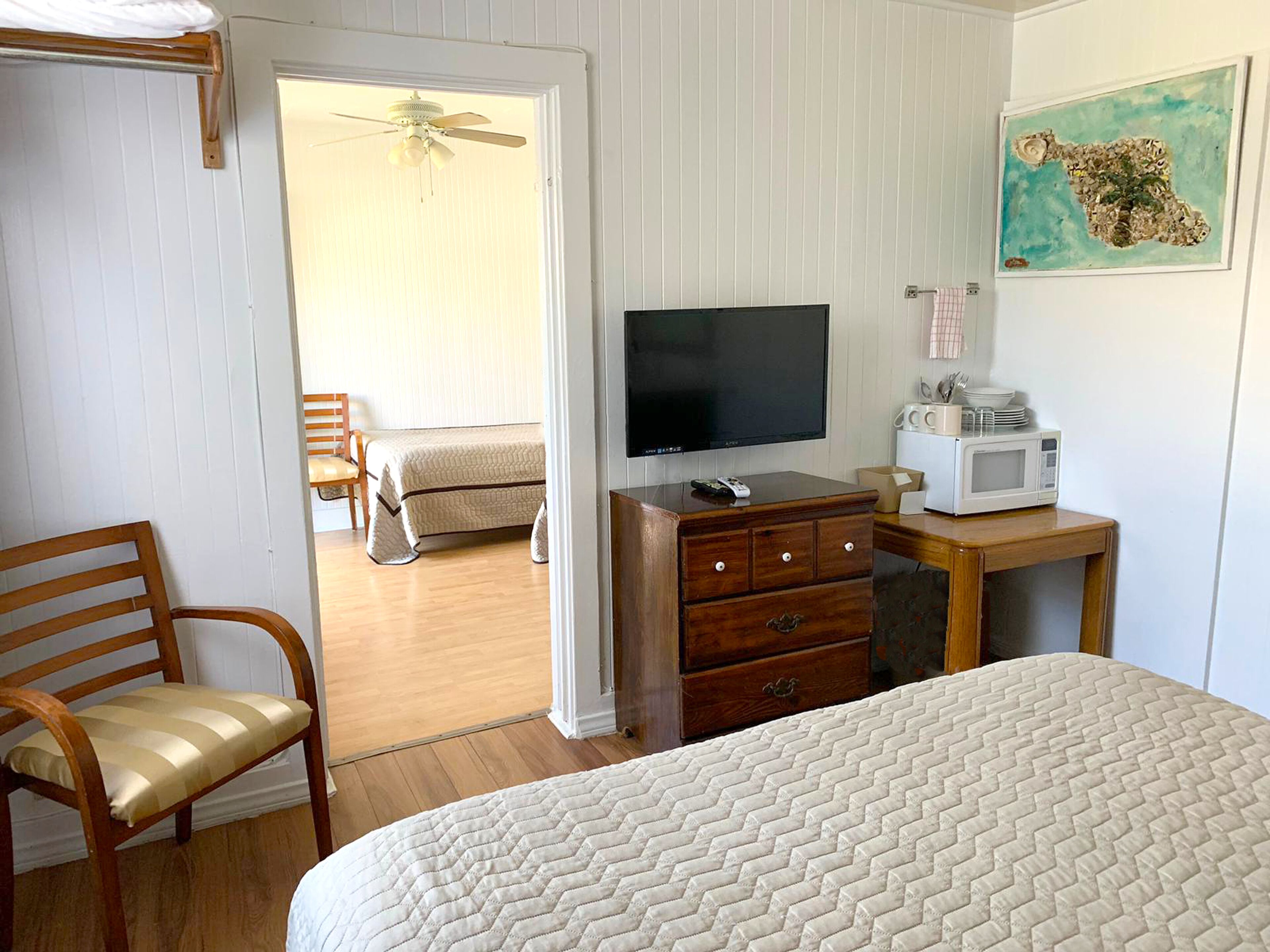 A bedroom with a bed, a television, a wooden dresser, a chair, and a ceiling fan.