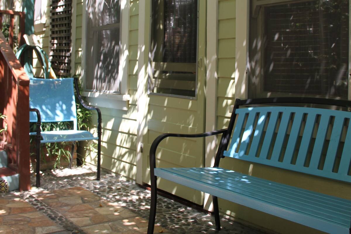 A covered porch with a stone floor, a blue bench, and a table with a blue tablecloth.
