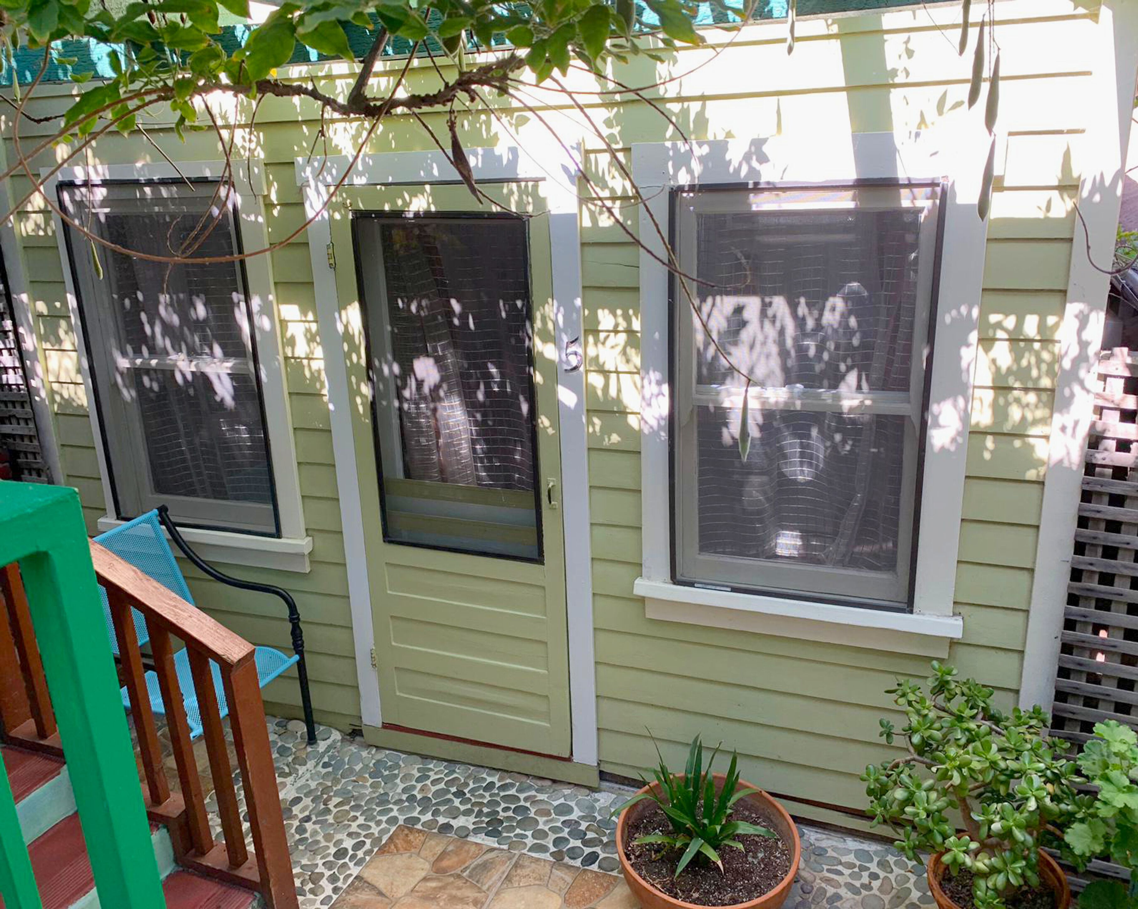 A house with three windows, a door, and a small garden area with potted plants.