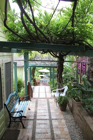 A covered patio area with a bench, potted plants, and a table under a pergola.