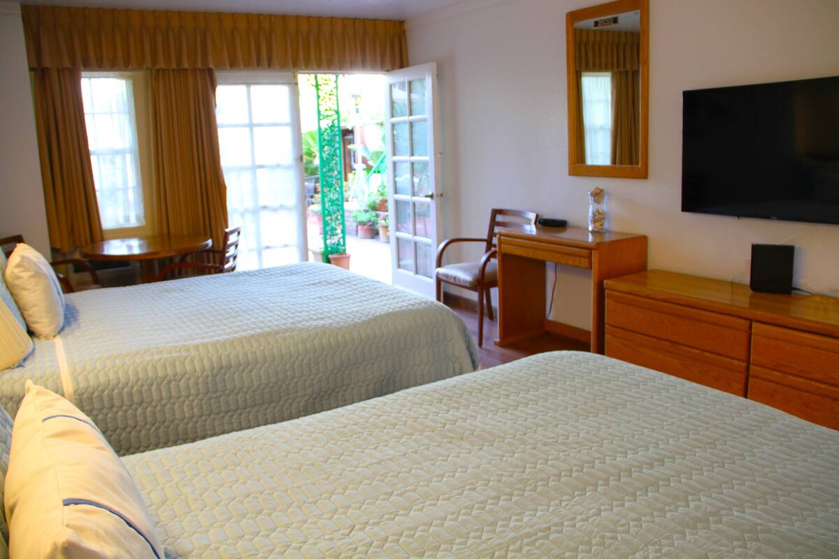 A hotel room with two beds, a desk, a chair, a television, and a view of the outdoors.