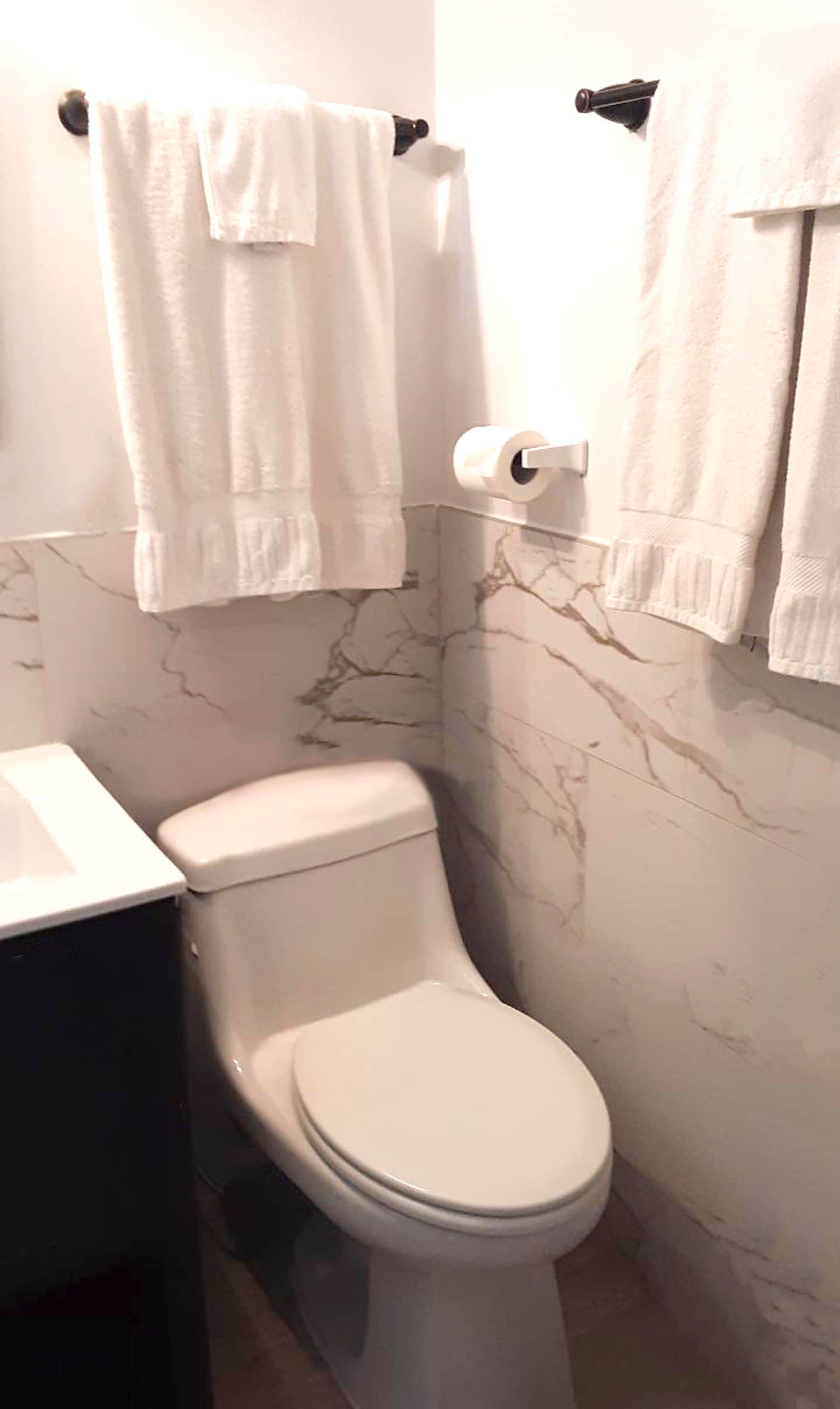 A bathroom with a toilet, marble walls, and white towels hanging on a rack.