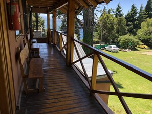 A wooden deck with a railing overlooking a grassy area and a body of water. - Apart Hotel del Arroyo (San Carlos de Bariloche)