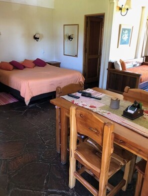 A room with a bed, a wooden table with chairs, a small table with a lamp, and a door. - Apart Hotel del Arroyo (San Carlos de Bariloche)