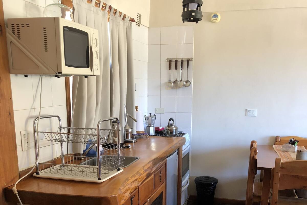 A kitchen with a stone-tiled floor, wooden cabinets, a built-in microwave, and a dining area with a wooden table and chairs.