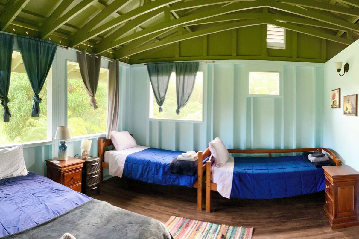 Une chambre avec deux lits, une commode en bois, une petite table et une fenêtre avec des rideaux.
