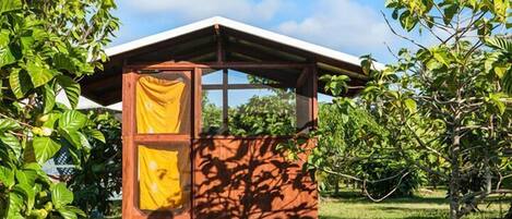 Una pequeña estructura de madera con techo inclinado, rodeada de abundante vegetación.