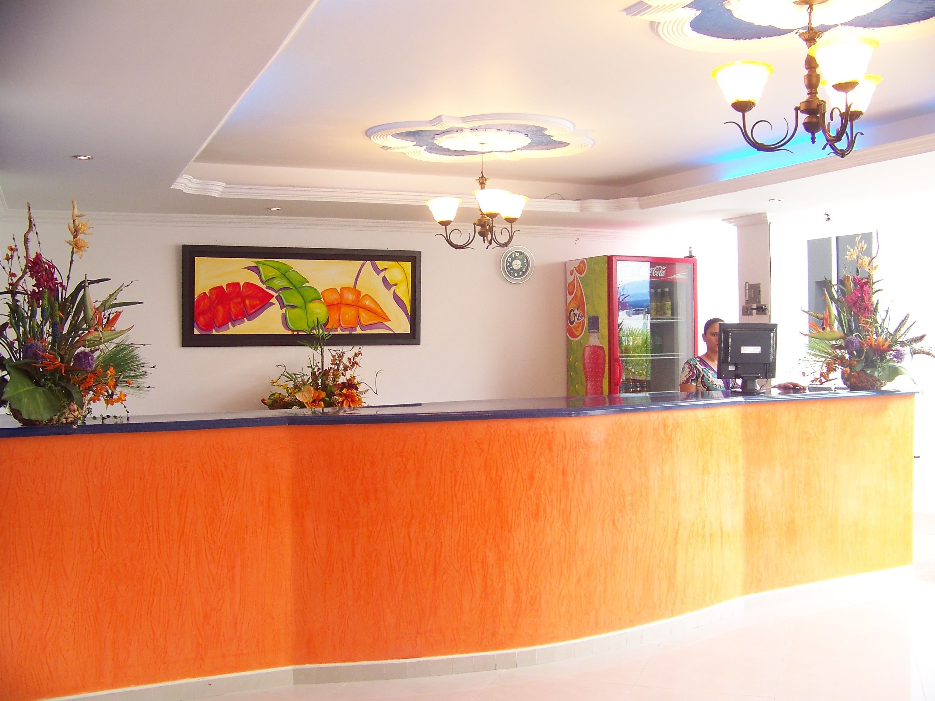 Zona de recepción con un mostrador de madera, una obra de arte floral enmarco y un refrigerador Coca-Cola.