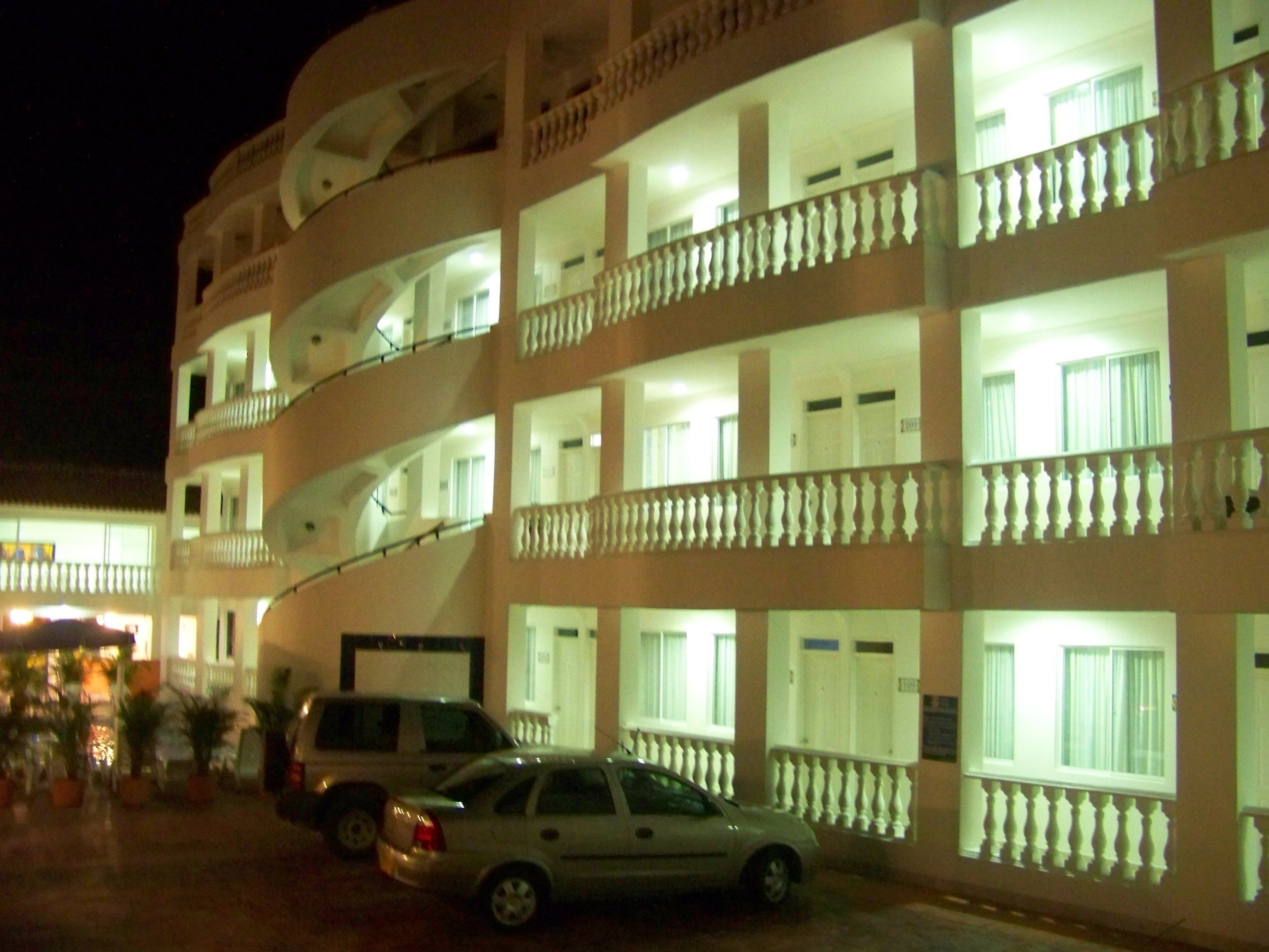 Un hotel de varios pisos con balcones, un estacionamiento y un coche estacionado al frente.