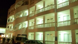 A multi-story hotel with balconies, a car parked in front, and a well-lit facade.