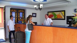 A reception desk with a wooden finish, a clock on the wall, and a framed painting of tropical flowers.