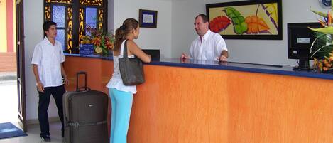A reception desk with a wooden finish, a clock on the wall, and a framed painting of tropical flowers.