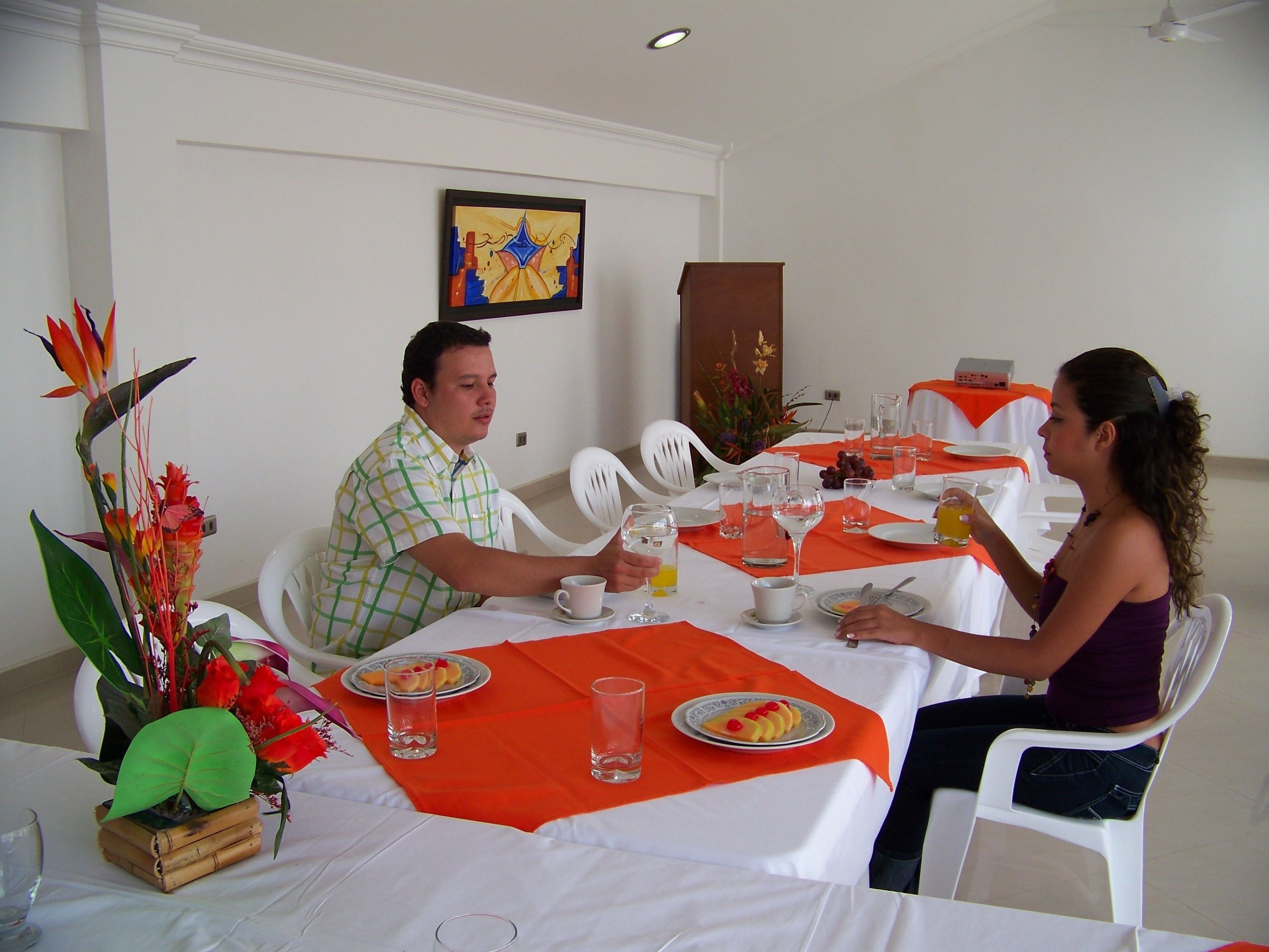 A dining table with white tablecloths, orange placemats, and a floral centerpiece.