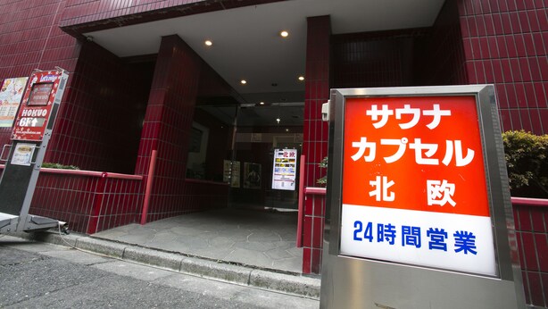 A building entrance with a sign indicating a 24-hour business operation. - Sauna & Capsule Hokuoh - Cators to Men (Tokyo)