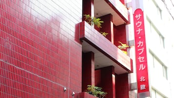 Un edificio rojo con varios balcones, algunos adornados con plantas. Hay señalización en el suelo y un letrero vertical en la fachada.