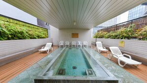 A rooftop pool area with a glass table and white chairs, surrounded by tiled walls and greenery. - Sauna & Capsule Hokuoh - Cators to Men (Tokyo)