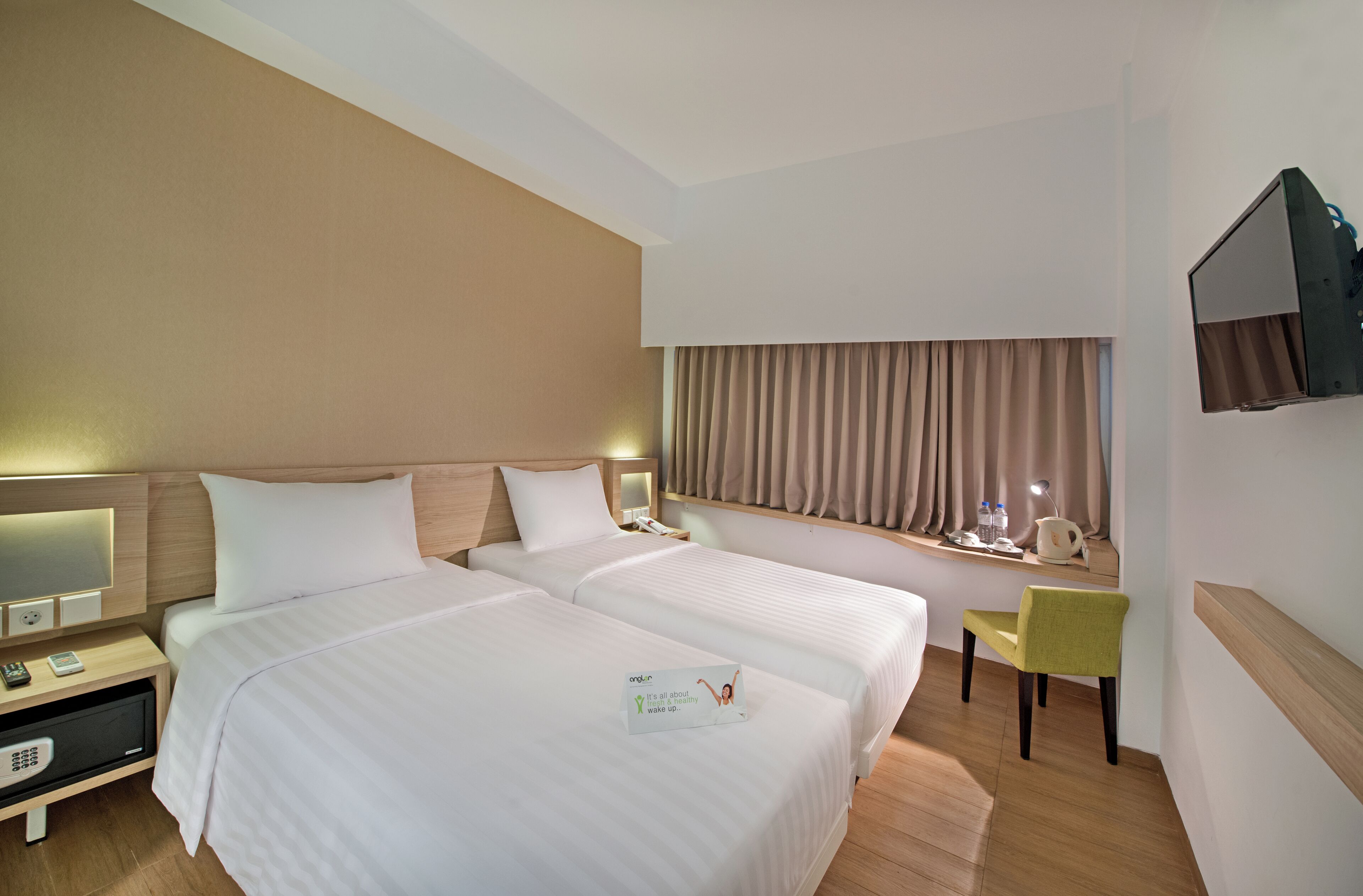 A hotel room with two beds, a desk, a chair, a TV, and a window with curtains.