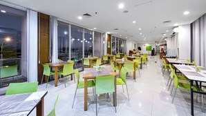 Zona pranzo moderna con sedie verdi e tavoli in legno, ampie finestre e interni luminosi.