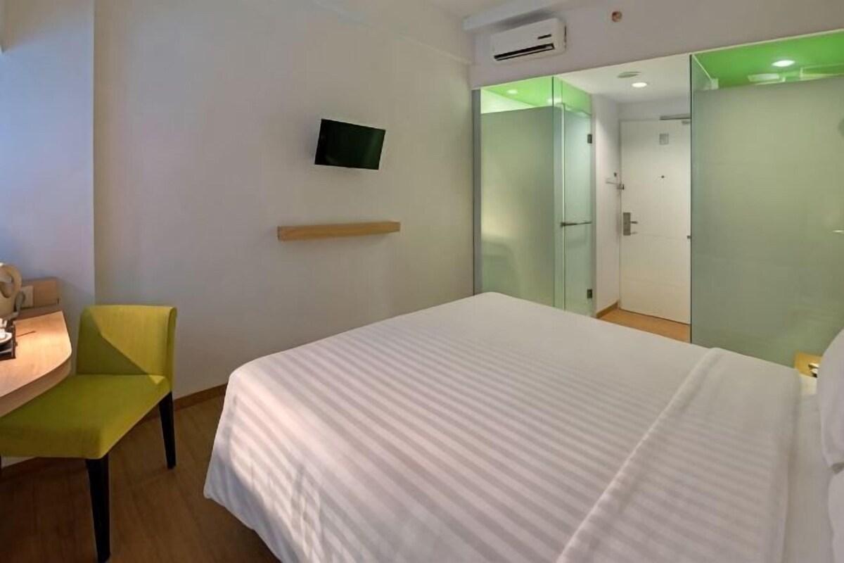 A hotel room with a bed, a desk with a chair, a television, and a mirror.