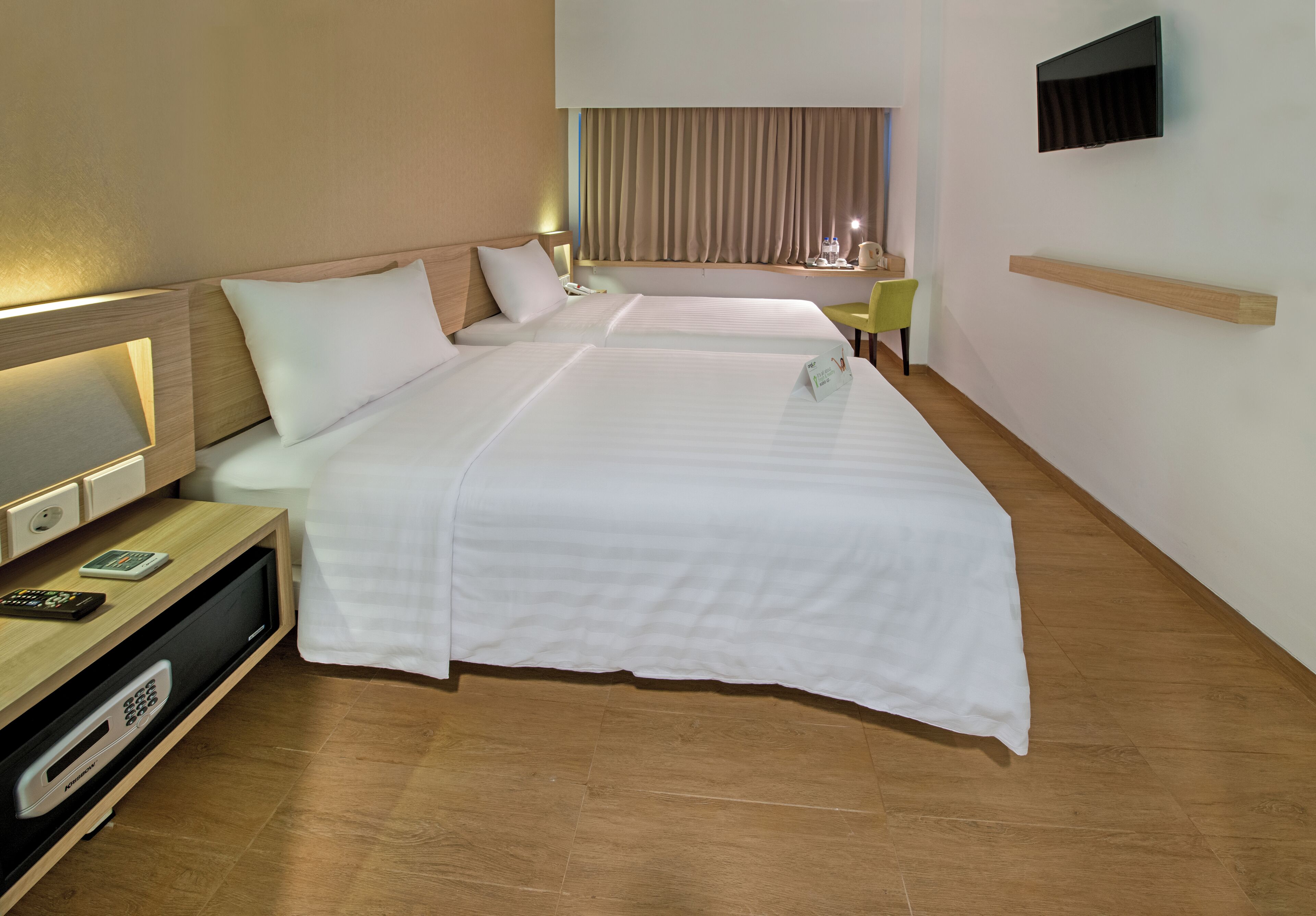 Quarto de hotel com duas camas, uma mesa de trabalho com televisão, uma cadeira e uma janela com cortinas.